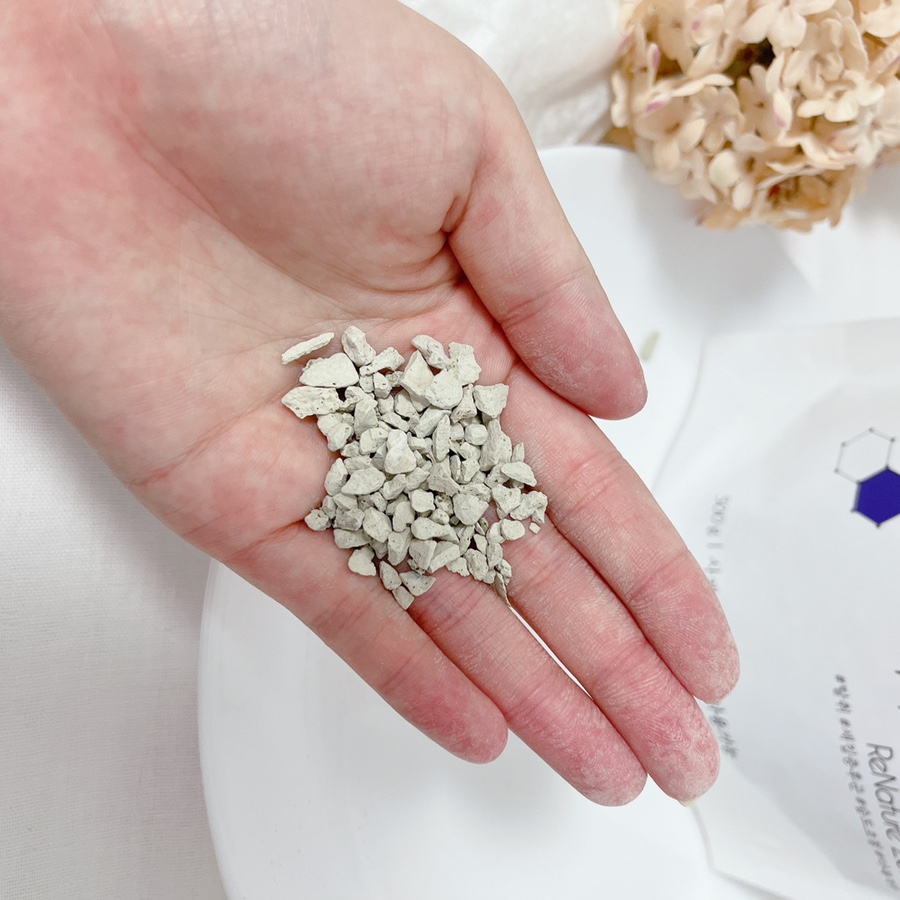 Close-up of a hand holding zeolite beads beside a water quality report and charts on a clean desk