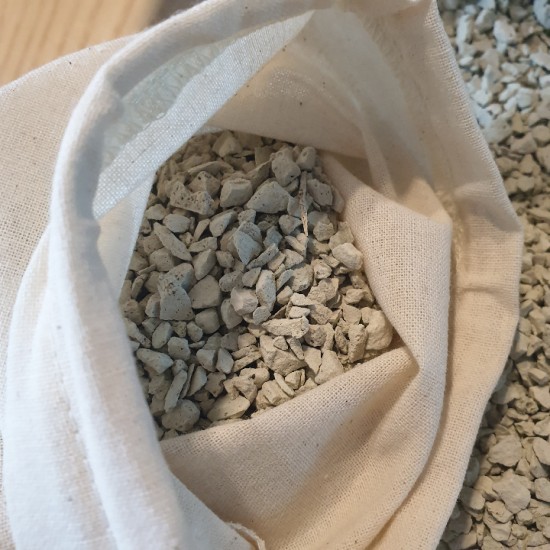 Close-up of a breathable fabric pouch filled with white zeolite granules placed on a sunlit windowsi