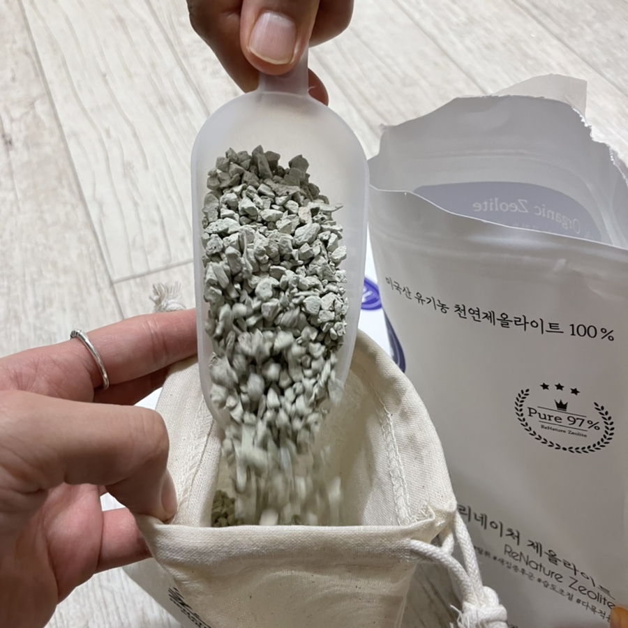 Close-up of hands pouring natural zeolite beads into an aquarium filter with a measuring cup nearby