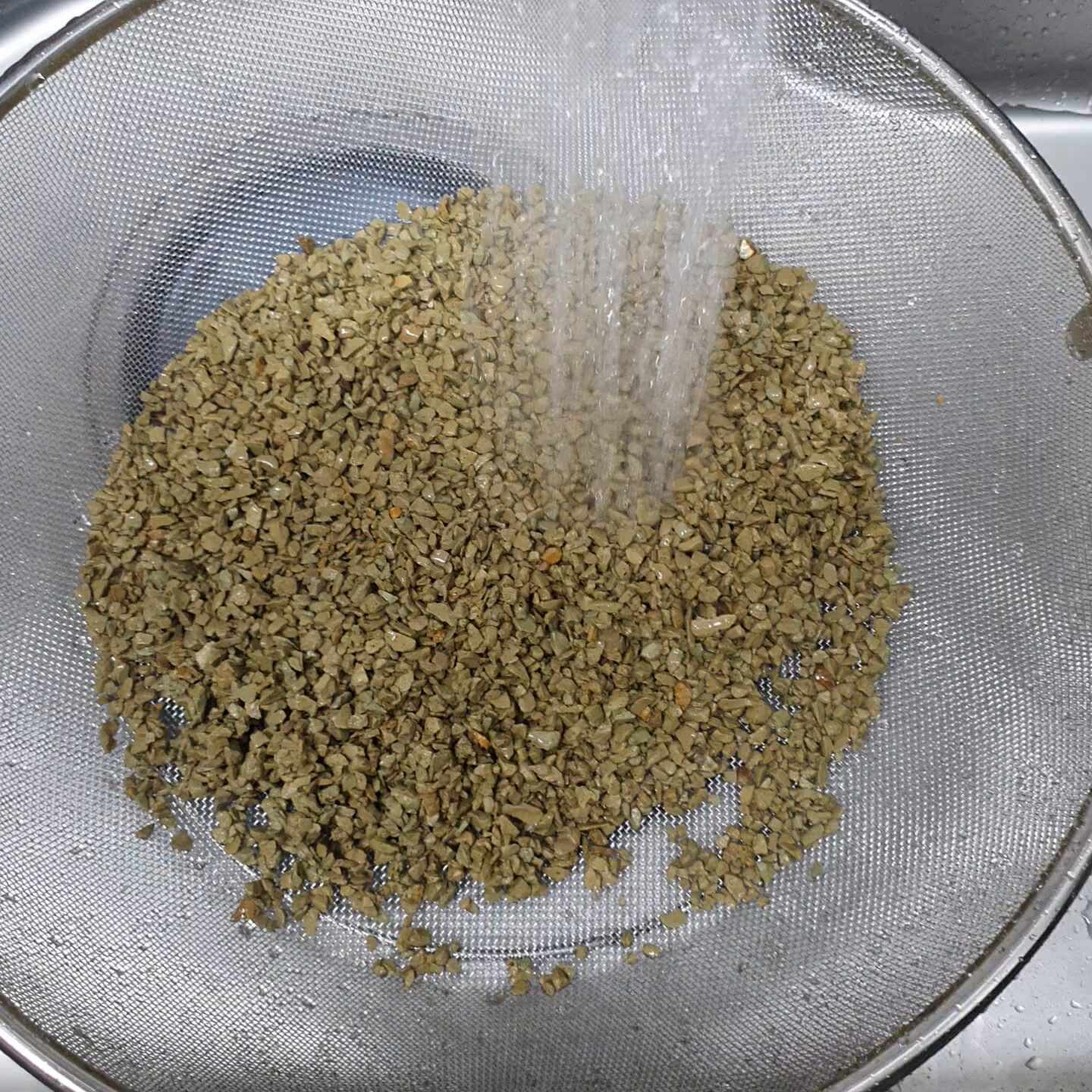 Beads being rinsed under cold running water in a transparent sieve, droplets illuminated by light, n