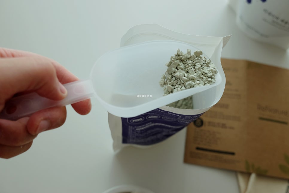 Hand pouring a small amount of white powder into a glass of water, placed near a kitchen scale and t